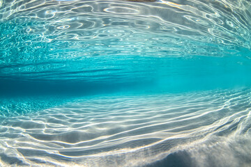 Crystal-clear waters with intricate light patterns on the sandy floor, captured underwater at Jervis Bay, Australia.