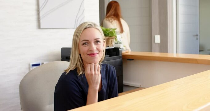 Smiling woman sitting at reception desk in medical clinic, looking at camera