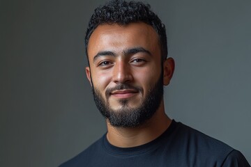 A young man with a beard smiles confidently in a portrait setting.