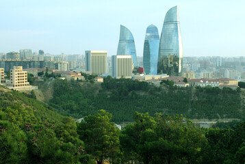 Daytime view of the iconic Flame Towers rising above the cityscape, with surrounding historic buildings and greenery in the foreground.