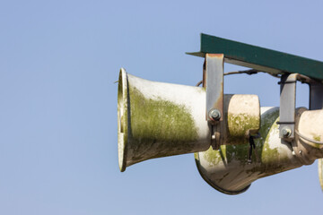 A close-up of an old, rusty megaphone covered in green moss. The megaphone is mounted on a metal...