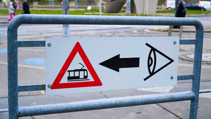 Warning sign directing pedestrians towards the left for tram traffic in an urban setting