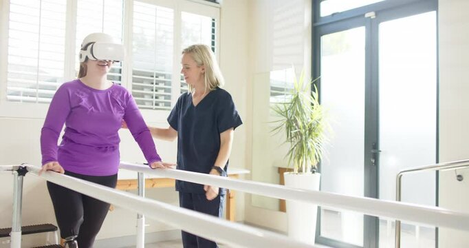 Woman in prosthetic leg walking using VR headset with therapist on parallel bars