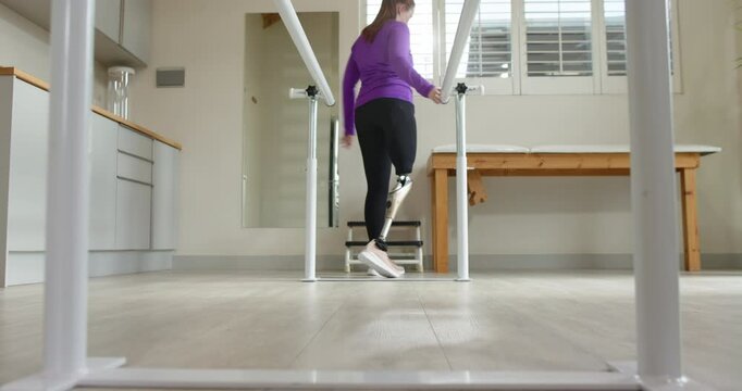A woman with prosthetic leg walking between parallel bars in a rehab room