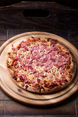 Pizza with ham and mozzarella cheese on wooden background. Soft focus. Close up