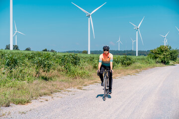 Obraz premium Cyclist enjoying a sunny day on a gravel path surrounded by wind turbines in a rural landscape