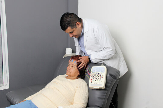 Elderly Latin woman undergoes EEG electroencephalogram to detect dementia or Alzheimer's disease in office with dark-skinned specialist doctor