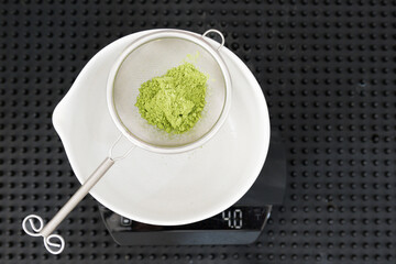 Barista making green tea in to white cup at the coffee shop.Close up strainer while preparing matcha menu from green tea powder on black background.