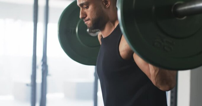 Lifting heavy barbell, man focusing on strength training in gym
