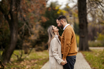 Side view of affectionate couple in love holding hands and looking at each other in city park.