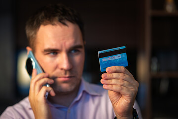 Businessman business man talking on phone during call hold card. young man in a pink shirt is dictating CVC code from a card to a phone fraudster. bank customer support by phone.