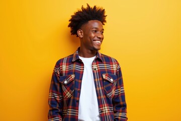 Fototapeta premium Cheerful Young Man with Afro Hair Smiling Against Bright Yellow Background, Wearing Plaid Shirt, Expressing Joy and Confidence