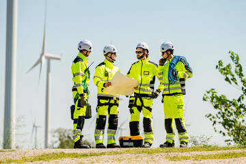 Safety team discusses plans for maintenance work on wind turbines at a renewable energy site during the day