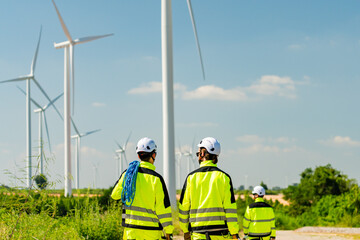 Workers in bright gear inspect wind turbines in a renewable energy field on a sunny day