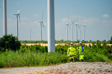 Workers inspect renewable energy site with wind turbines during sunny day in rural area