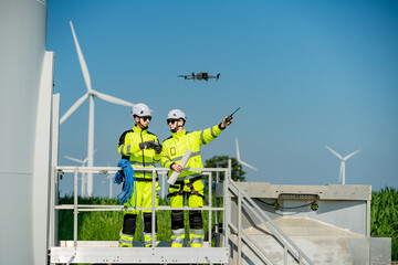 Engineers operate drone for inspection at a wind farm under clear blue sky with wind turbines in the background