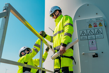 Workers conduct maintenance on a wind turbine in bright yellow safety gear under clear blue skies