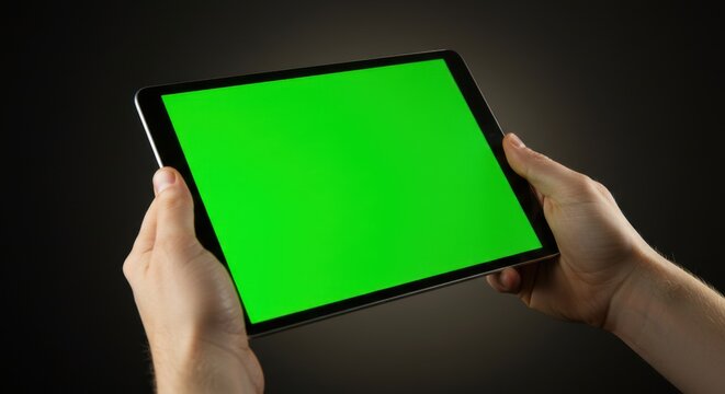 Hands holding a tablet computer with a green screen against a dark background. Ideal for showcasing apps, websites, or presentations - Powered by Adobe