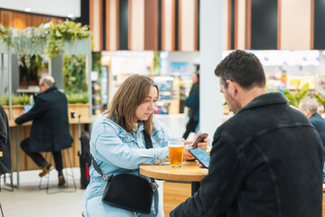 Man and woman looking at phones as they have a beer in the airport bar