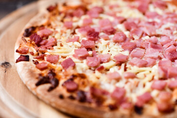 Pizza with ham and mozzarella cheese on wooden background. Soft focus. Close up