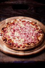 Pizza with ham and mozzarella cheese on wooden background. Soft focus. Close up