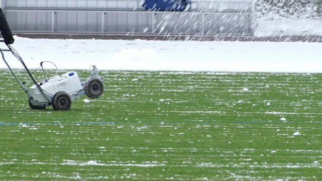 Groundsman removing snow from soccer field with line marking machine