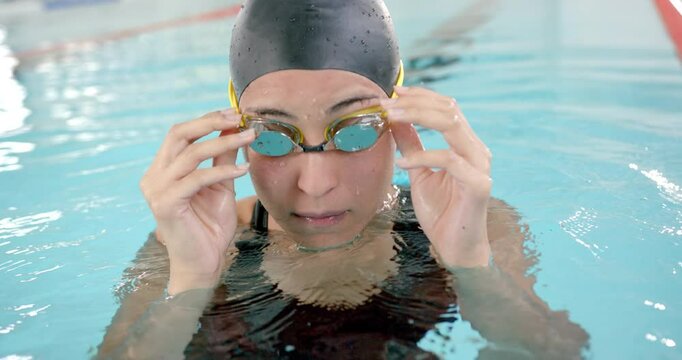 female swimmer adjusting goggles while training in indoor pool, preparing for swim
