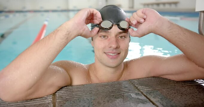 Smiling male female swimmer adjusting goggles while resting at edge of indoor pool