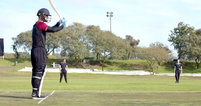 Two teams of multiracial male cricket players and male umpire playing cricket on pitch