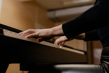 Close up view of gentle female hands with small ring in black clothes playing piano her favorite classical music, learning new melody, taking lessons. Romantic beige subdued light. Bottom view
