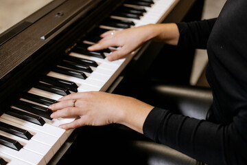 Obraz premium Close up view of gentle female hands with small ring in black clothes playing piano her favorite classical music, learning new melody, taking lessons. Romantic beige subdued light. Top view