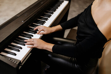 Fototapeta premium Close up view of gentle female hands with small ring in black clothes playing piano her favorite classical music, learning new melody, taking lessons. Romantic beige subdued light. Top view