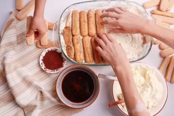 Kids hands placing savoiardi biscuits on cream to make tiramisu