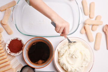 Child’s hand adding cream to tiramisu ingredients in a glass bowl