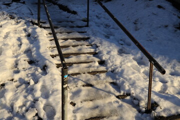 Winter staircase with handrails and steps under snow and ice illuminated by the sun
