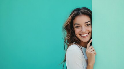 Fototapeta premium A portrait of a happy and smiling businesswoman peeking out from behind the edge, standing and holding an empty mint green wall with copy space area for your text or message.