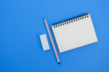 Blank grid notebook open near pencil and eraser, minimalistic stationery arrangement for note-taking, drawing, or creative writing, top view of clean workspace.