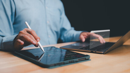 Person engages with tablet using stylus while simultaneously working on laptop, integration of modern technology in coding and digital productivity