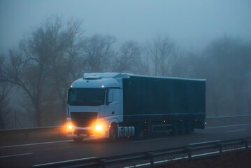 Truck driving on a highway on a day with adverse weather conditions due to fog, side view.