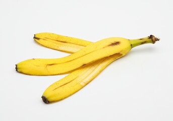 A single yellow banana peel slightly curled with visible brown spots isolated on a white background