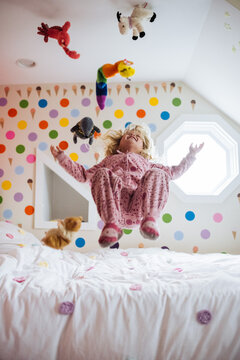 Girl and toys airborne jumping on bed