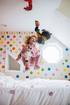 Girl jumping on bed with stuffed animals