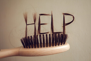 Hair Loss Concept: "HELP" Spelled with Strands on Brush. Wooden hairbrush with thinning hair spelling "help." Concept: hair loss, alopecia, health concerns.