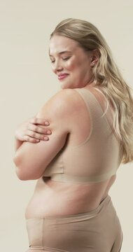 Vertical video: Smiling plus size woman in beige underwear embracing body positivity