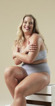 Vertical video: Smiling plus size woman in underwear embracing body positivity,