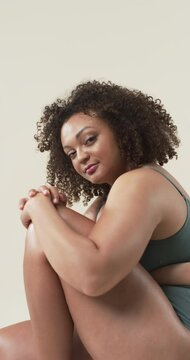Vertical video: Smiling plus size woman embracing body positivity, sitting confidently
