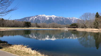 Snowy mountain reflected in tranquil park pond, clear sky, Japan