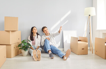 Happy young smiling couple sitting on floor with a lot of cardboard boxes in empty apartment...