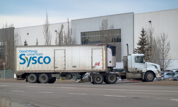 Calgary, Alberta, Canada. Jan 16, 2025. A Sysco semi-truck parked near a warehouse, featuring Good things come from Sysco branding and a small Canadian flag on the trailer.