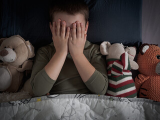 The boy hides under the covers in bed, trying to get rid of the nightmares and find solace in the...